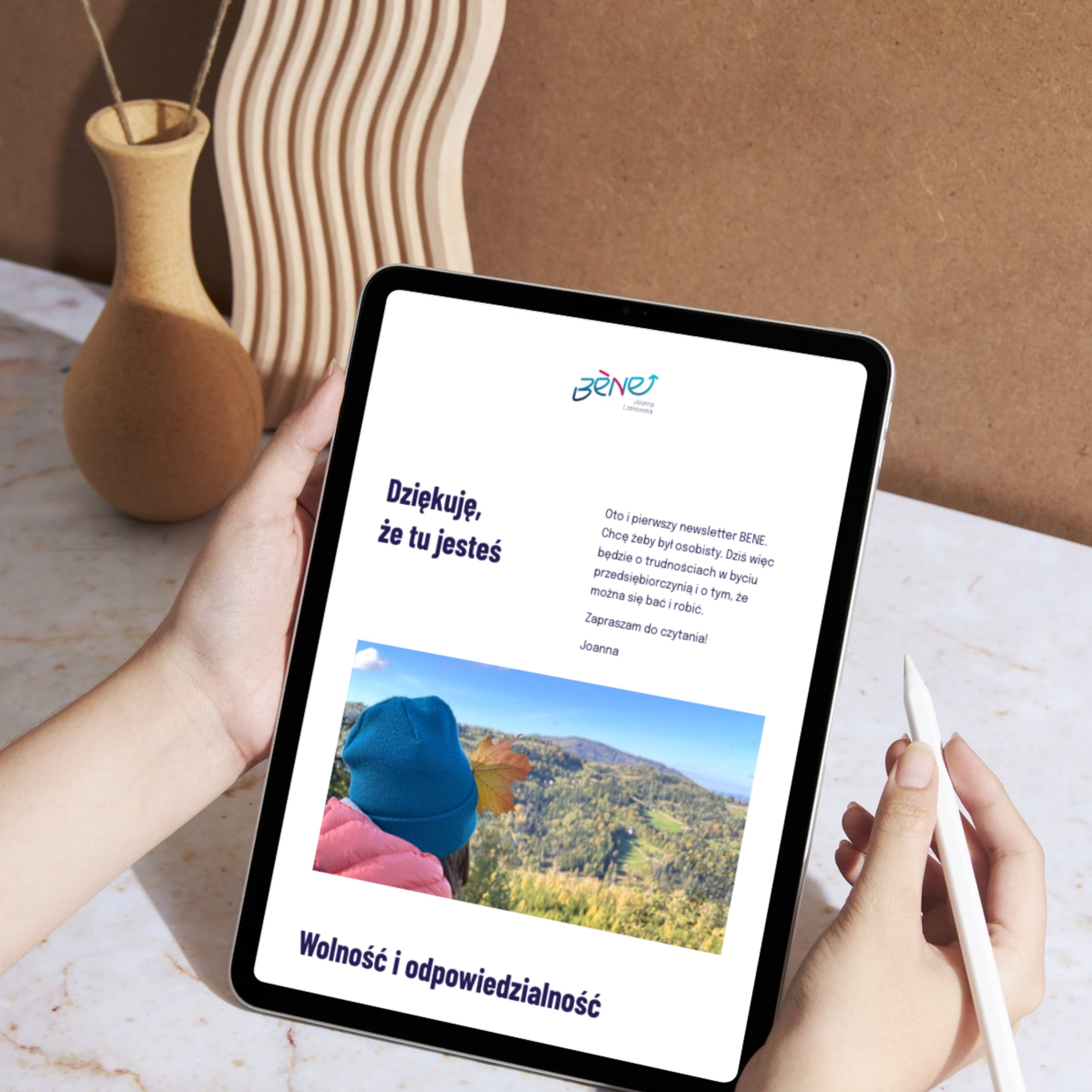 Ręce trzymają tablet w nim widać newsletter bene. Obrazek ilustracyjny.