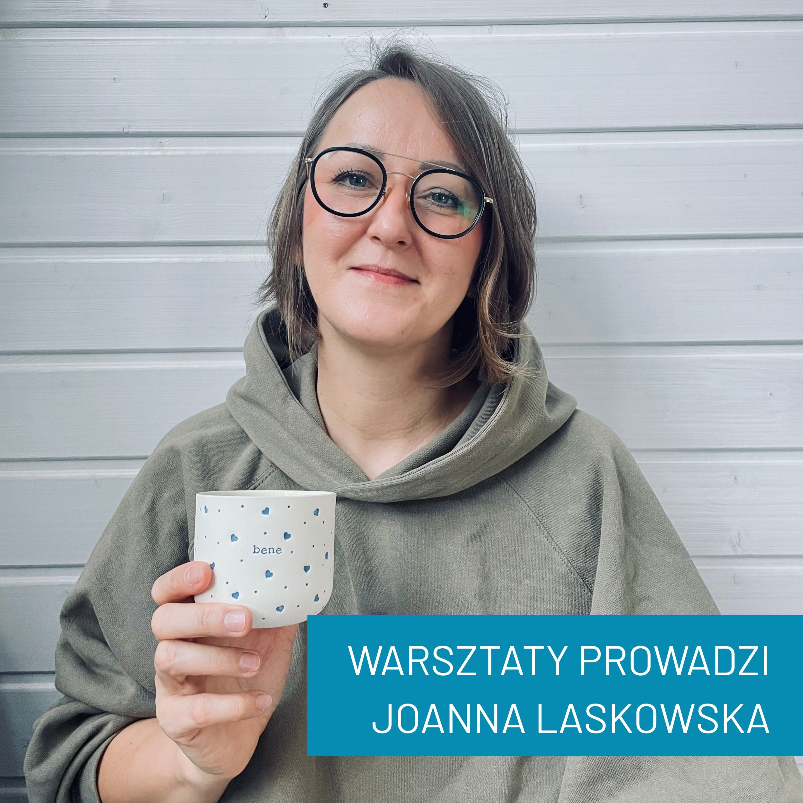 Portret Joanny Laskowskiej. Osoba jest uśmiechnięta, ubrana w bluzę z kapturem. W ręce trzyma kubek z napisem: bene.<br />
Podpis na zdjęciu: Warsztaty prowadzi Joanna Laskowska